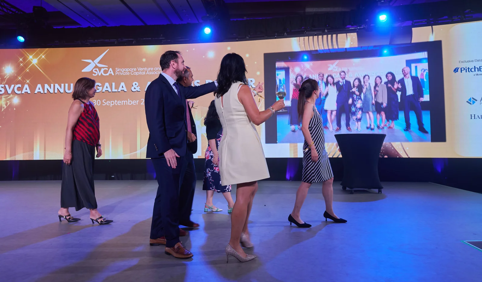 Gala guests turn towards their group photograph displayed on the large venue screen